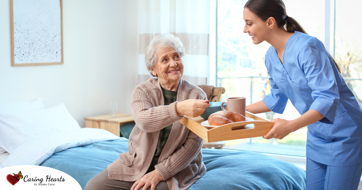 A professional caregiver smiles and provides food to an older adult in her care, representing the compassionate care needed for those with dementia.