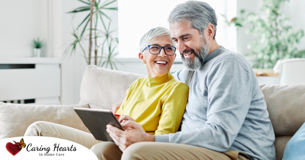 A senior couple smiles while looking at a laptop, showing how online resources can help family caregivers.