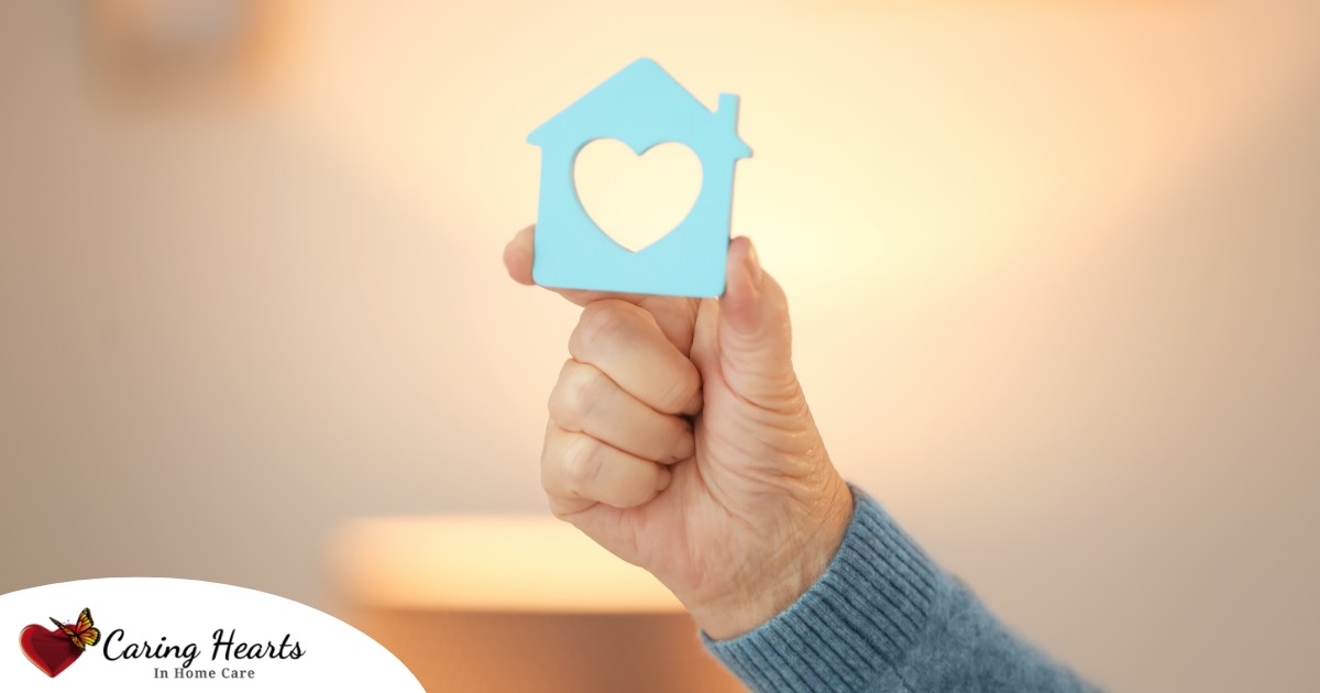 A hand holds up a cutout of a home with a heart in it, representing the home care industry.