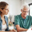 Adult daughter and senior father talking at a kitchen table while comparing home care vs assisted living